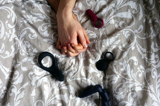 Couple holds hands on bed with adult toys